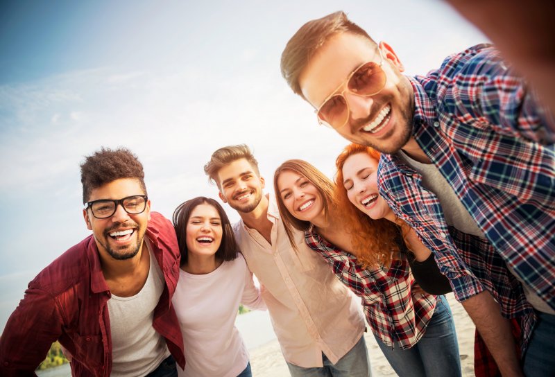 Patient smiling with their Invisalign on the beach surrounded by friends