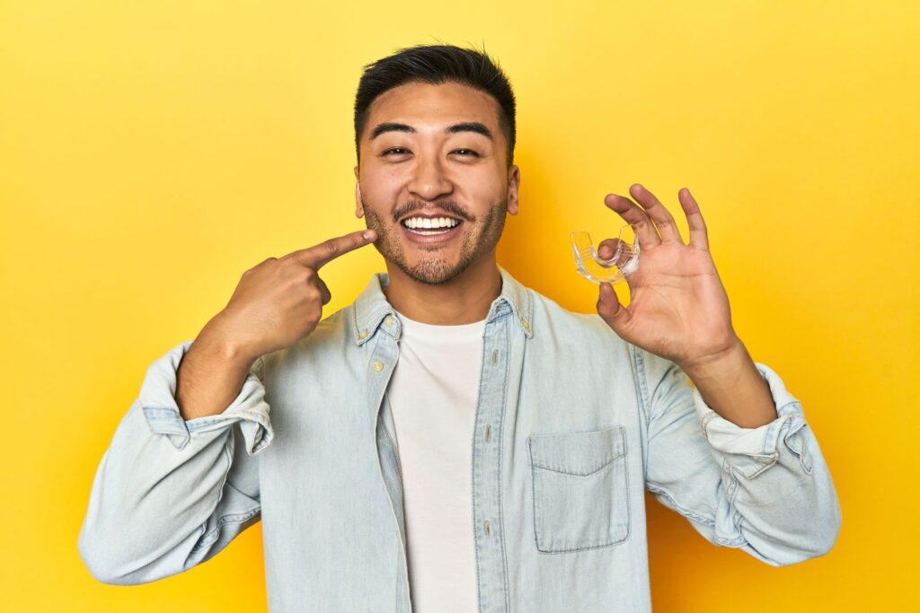 A man smiling and holding an Invisalign aligner.